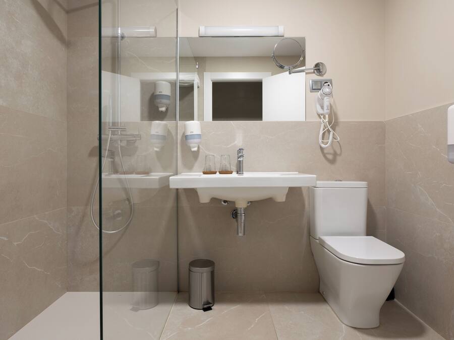 A modern bathroom with a glass-enclosed shower, a sink with soap dispensers, a toilet, and a hand dryer.