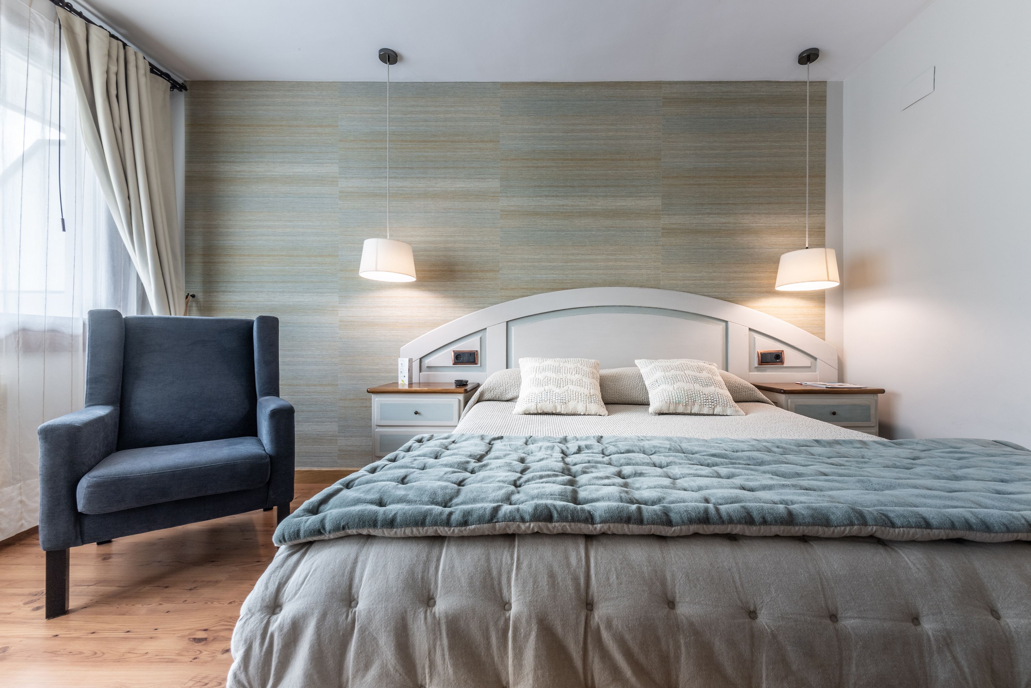 A bedroom with a bed, a chair, two bedside tables, and a wall with a textured pattern.