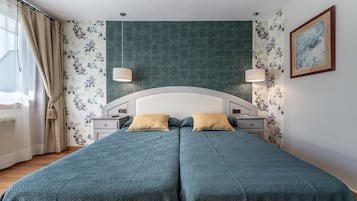 Una cama doble con colcha color aguamarina, dos mesitas de noche con lámparas, papel tapiz con motivos florales y un cuadro en la pared.