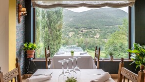 Mesa de comedor para cuatro con vistas panorámicas a la montaña, una planta en maceta y una lámpara en la pared.