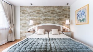 Un dormitorio con pared de piedra, dos mesitas de noche, una cama con colcha gris y un cuadro en la pared.