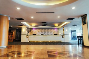 Uma área de recepção de hotel com piso de mármore, balcão de atendimento e parede com desenhos circulares.