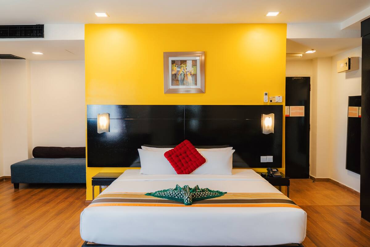 A hotel room with a bed, bedside tables, a wall-mounted artwork, and a red pillow.