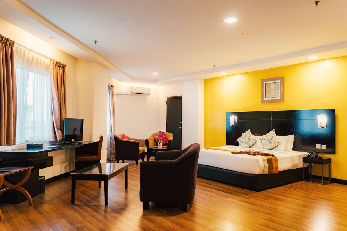 A hotel room with a bed, a desk with a computer, a chair, a small table, and a bedside table.