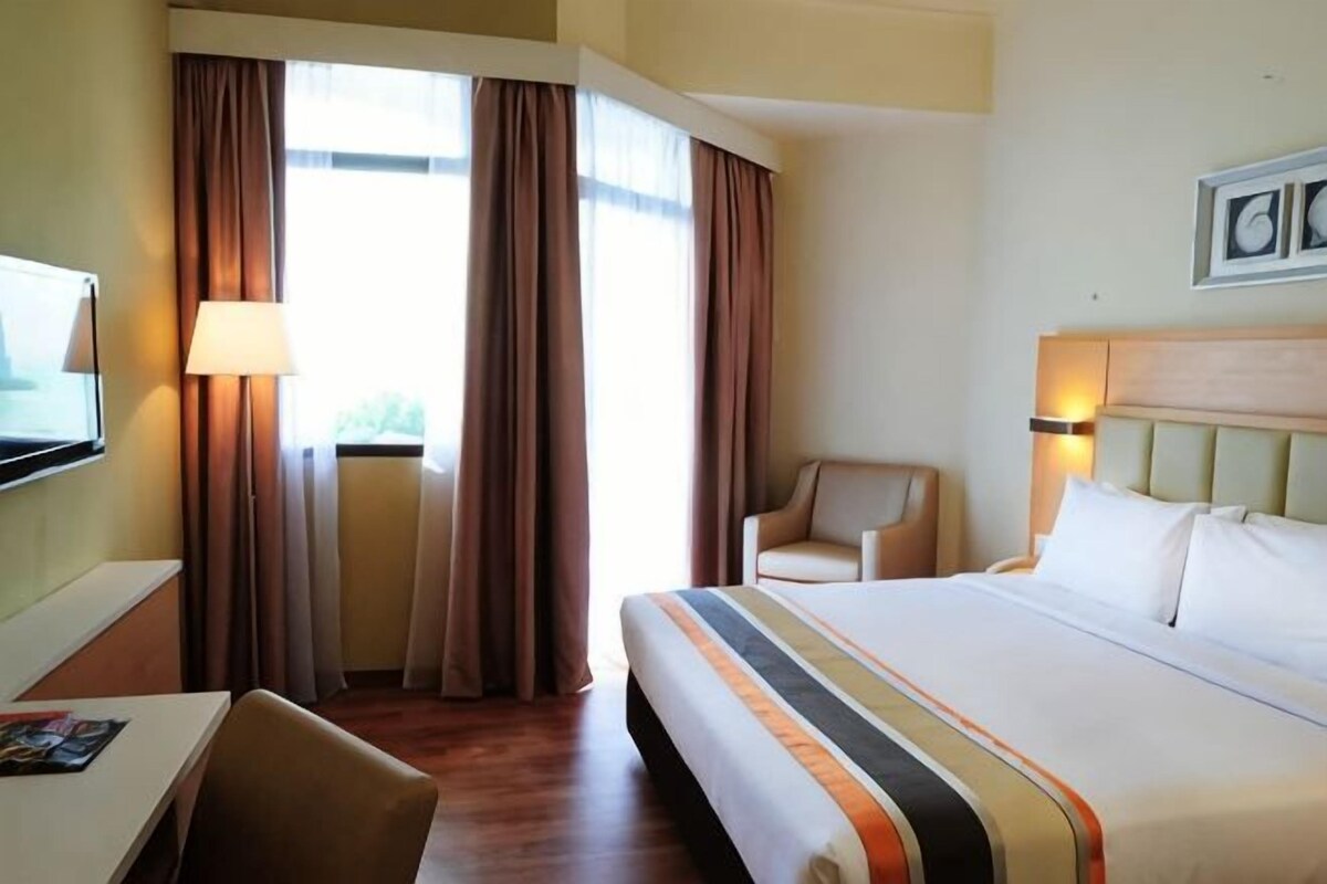 A hotel room with a bed, a desk, a chair, a TV, and a window with curtains.