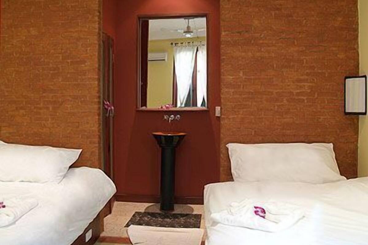 A hotel room with two beds, a small sink, and a mirror.