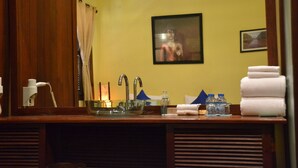 Un baño con un tocador de madera, un lavabo con un recipiente de vidrio, un espejo y un cuadro enmarcado en la pared.
