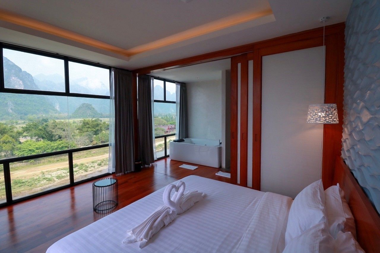 A hotel room with a large bed, a view of a mountainous landscape, a bathtub, and a wooden floor.