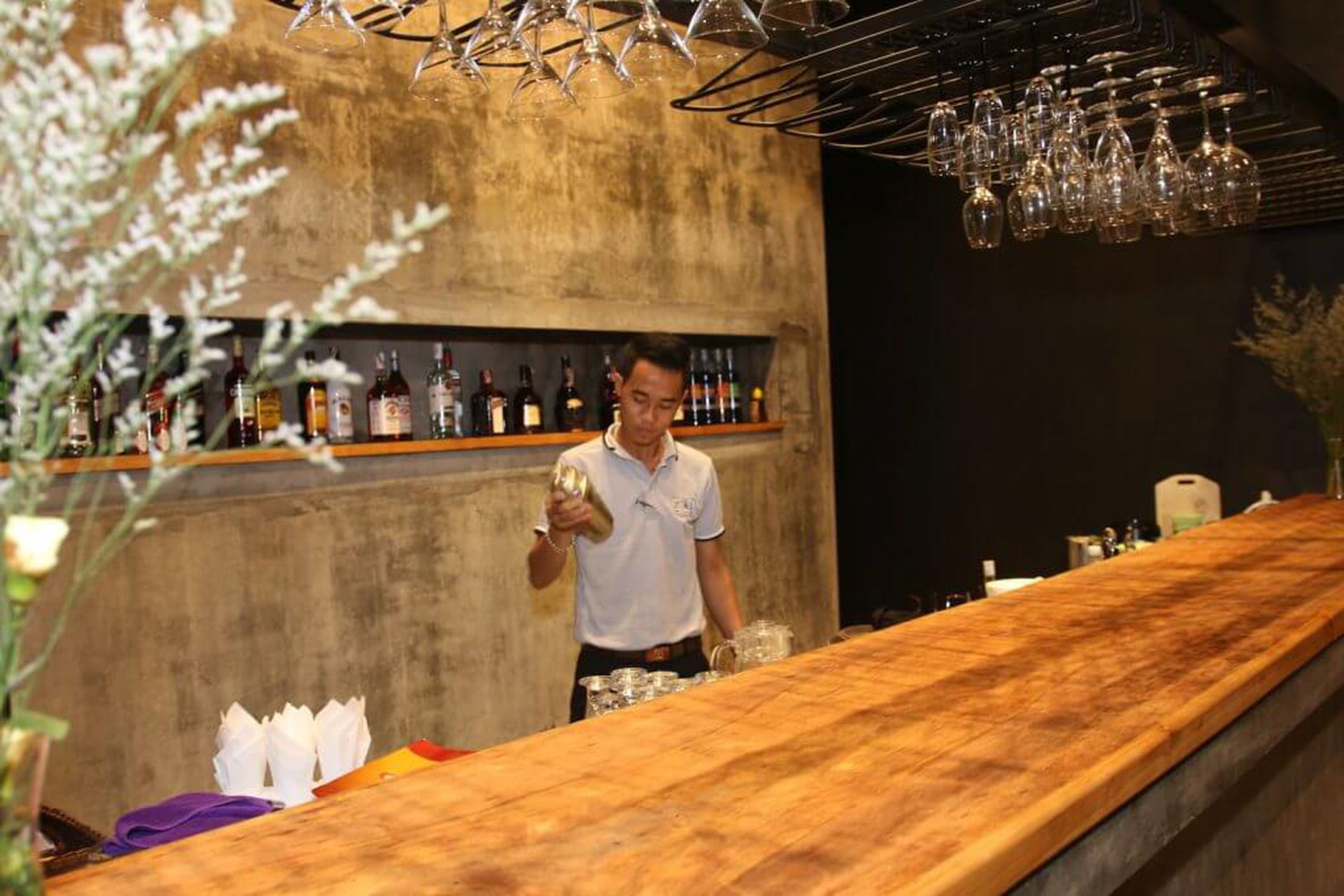 A bar area with a bartender, a wooden counter, and shelves with bottles.