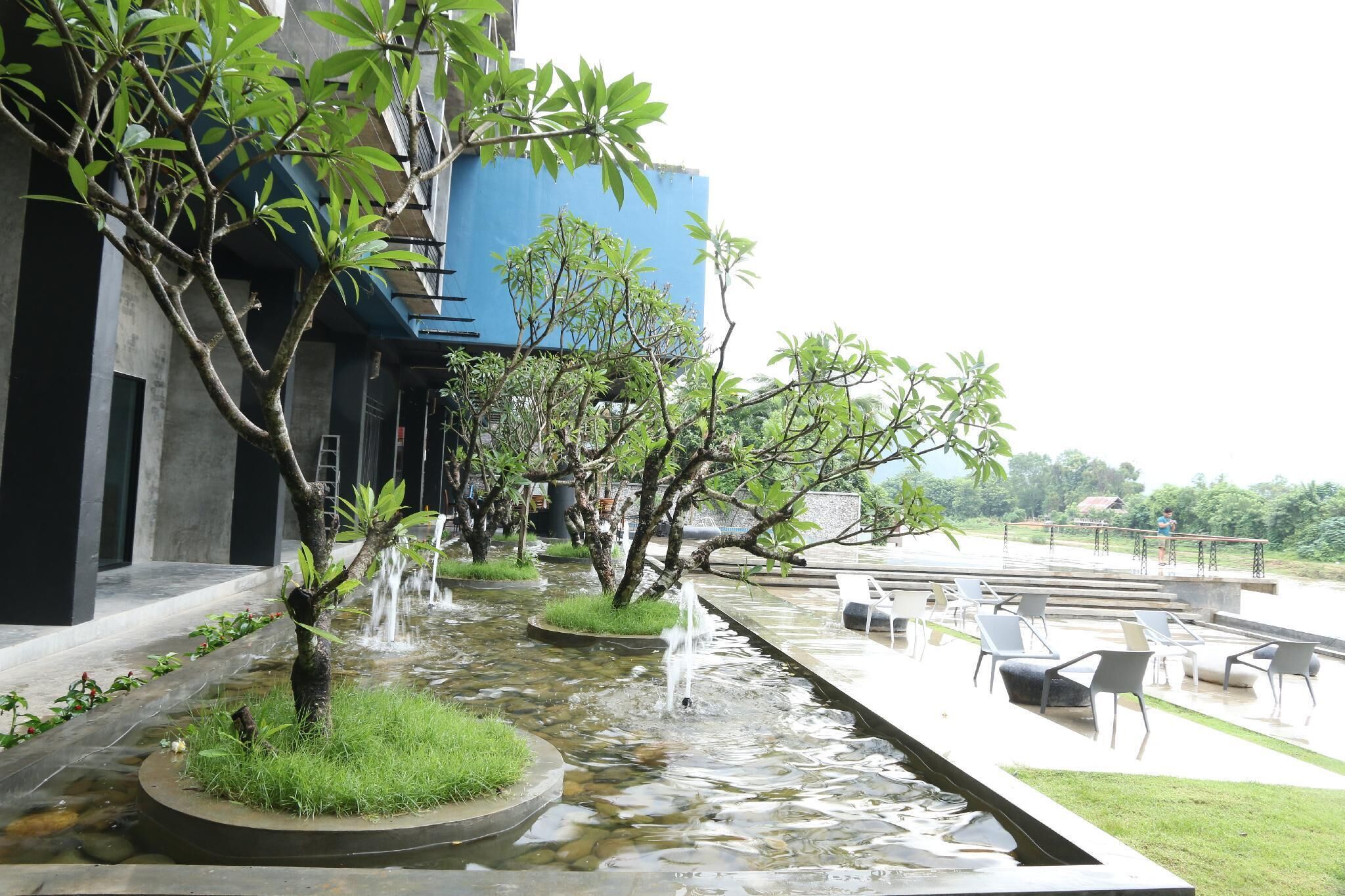 A water feature with multiple streams, a seating area with chairs, and a building with a blue facade.