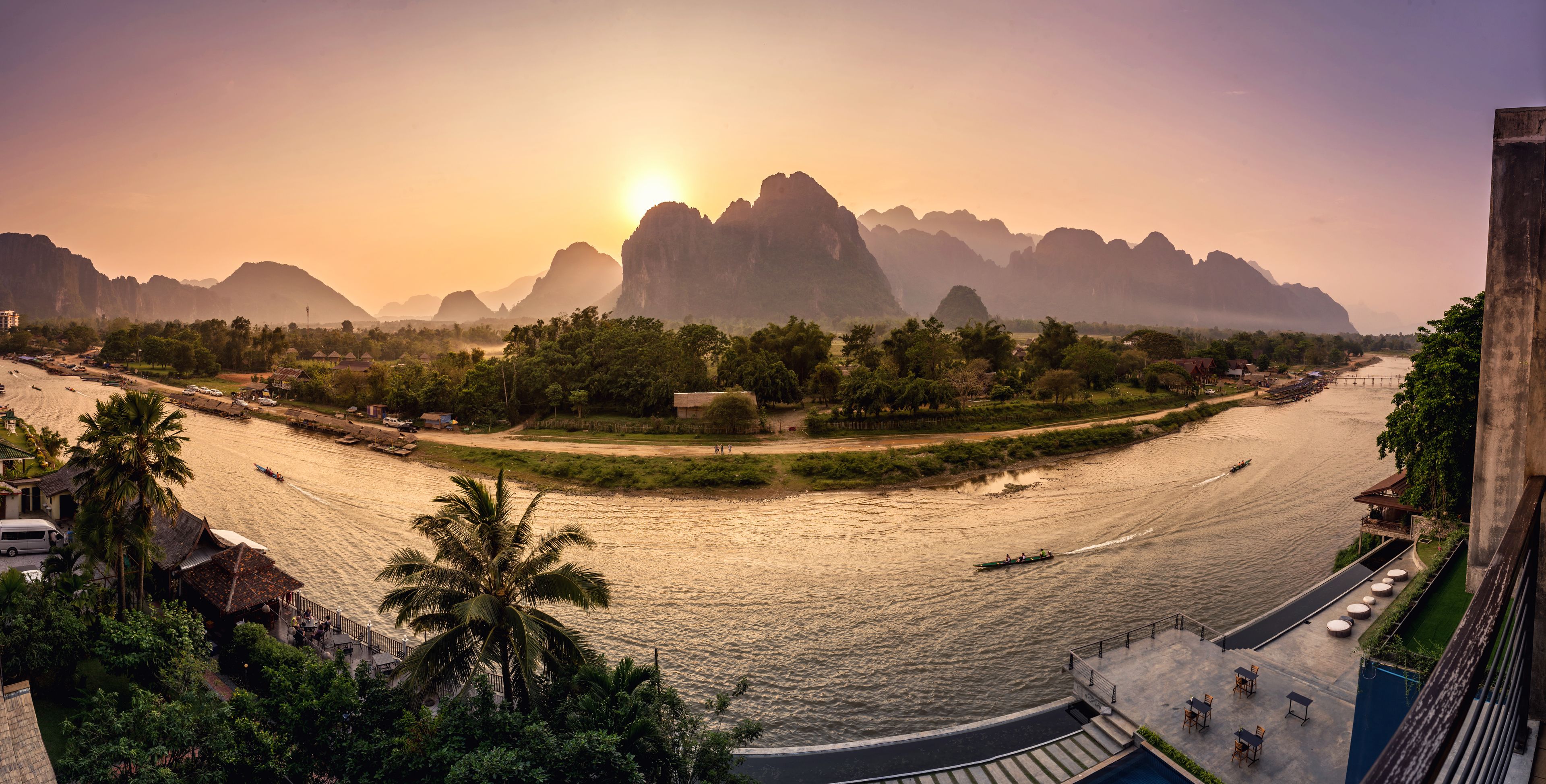 A riverside view with a bridge, palm trees, and distant mountains.