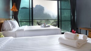 Habitación de hotel con dos camas, vista a la montaña a través de amplias ventanas y una mesita con toallas.