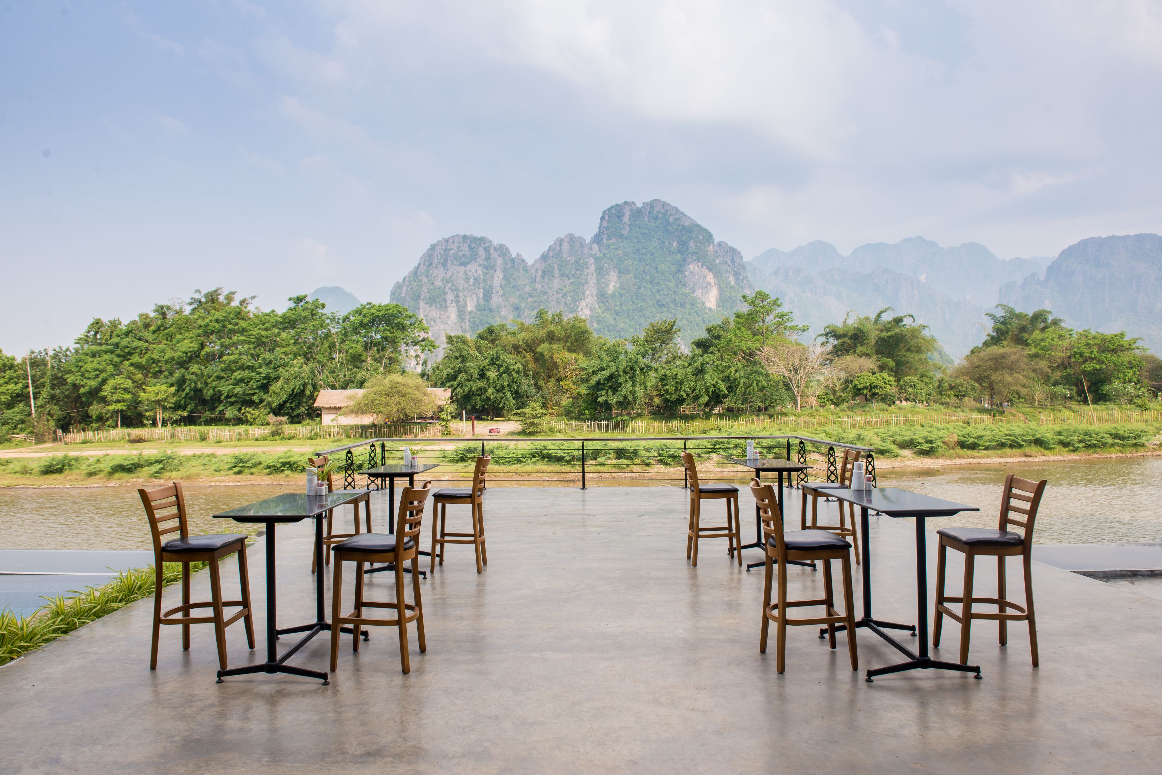 An outdoor dining area with tables and chairs, overlooking a river and mountains.