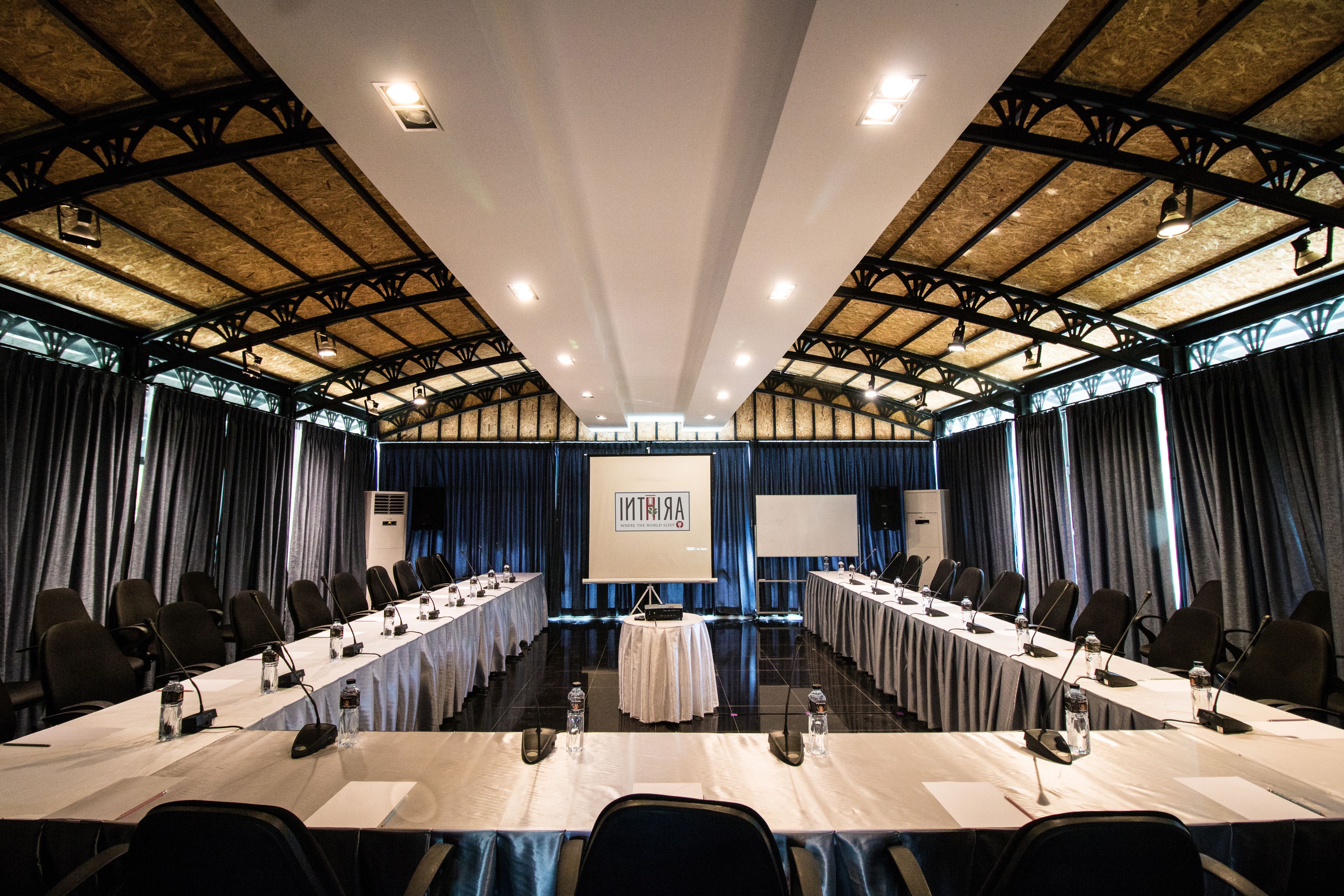 Una sala de conferencias con una larga mesa, sillas, micrófonos y una pantalla al frente.