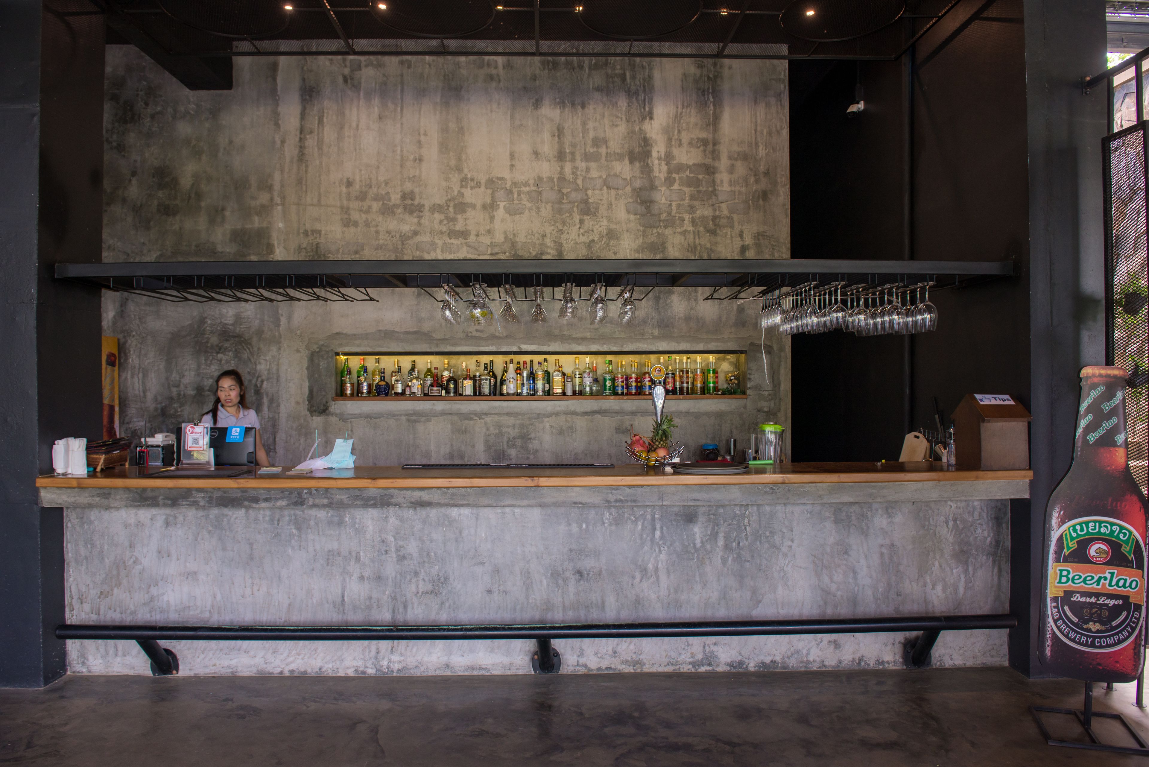Zona de bar con un cantinero, una barra con diversas botellas y una gran exhibición de botellas de cerveza.