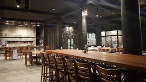 Un restaurante espacioso con una barra de madera larga, varias zonas de estar y una pared de acento de piedra.