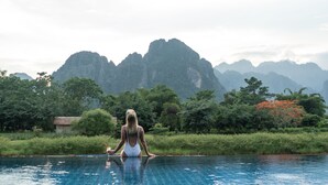 Una persona medita junto a una piscina con montañas al fondo.