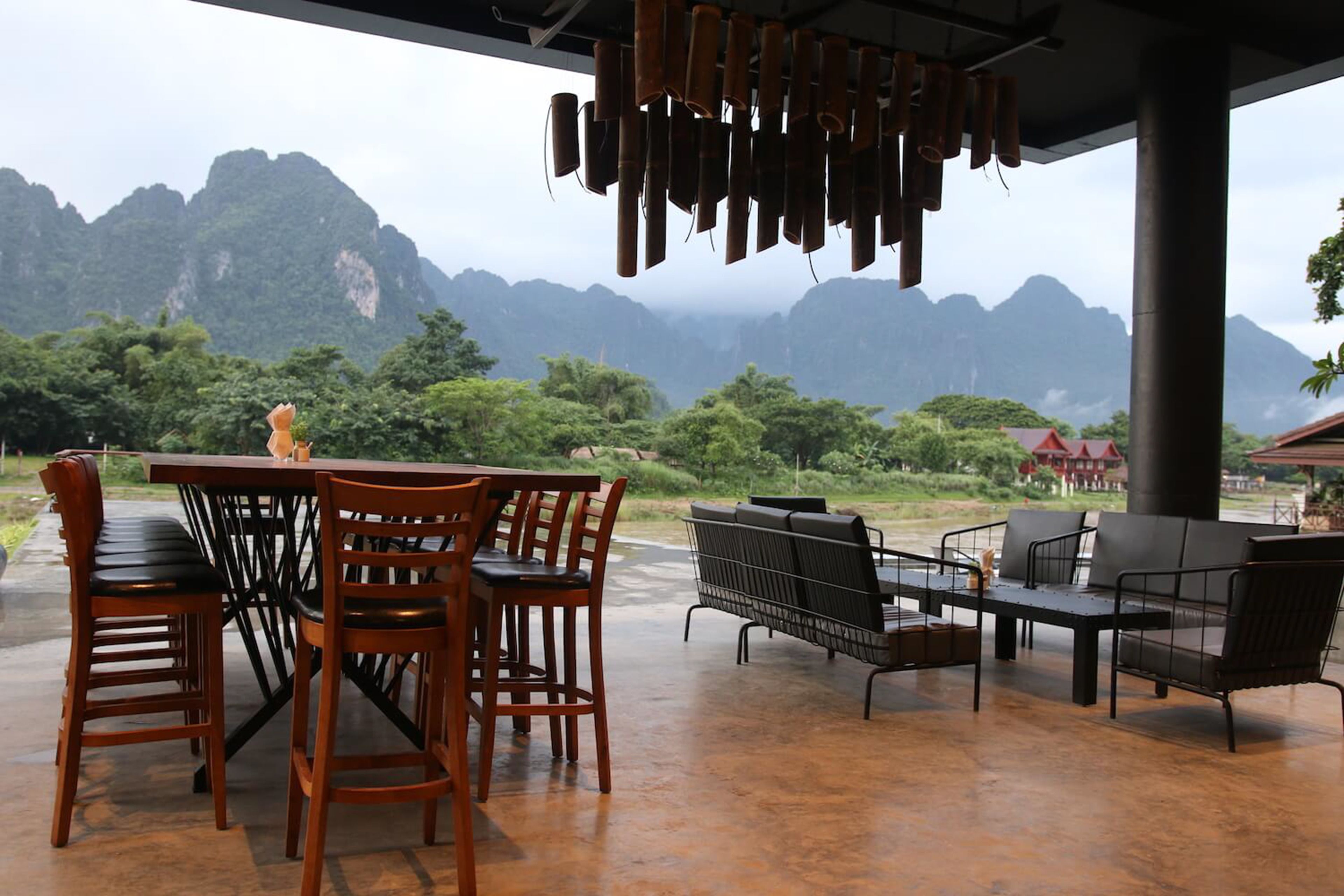 An outdoor dining area with wooden chairs and tables, overlooking a mountainous landscape.