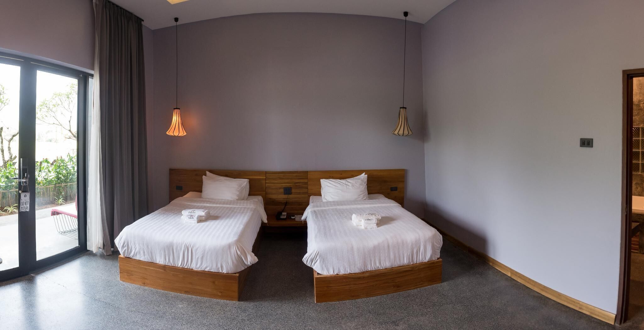 A hotel room with two beds, a large window, and a door leading outside.