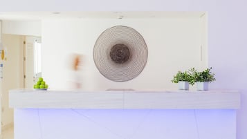 Un comptoir d’accueil agrémenté d’une grande œuvre d’art murale de forme circulaire, d’une plante en pot et d’une pile de pommes vertes.