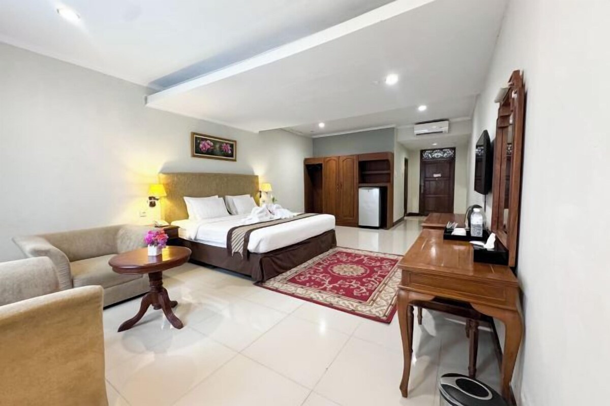 Habitación de hotel con cama, sofá, una mesita redonda, un escritorio de madera y televisor.