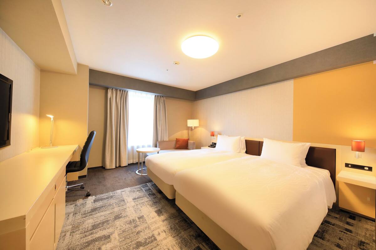 Une chambre d’hôtel avec un grand lit, un bureau, une chaise, une petite table et une lampe.