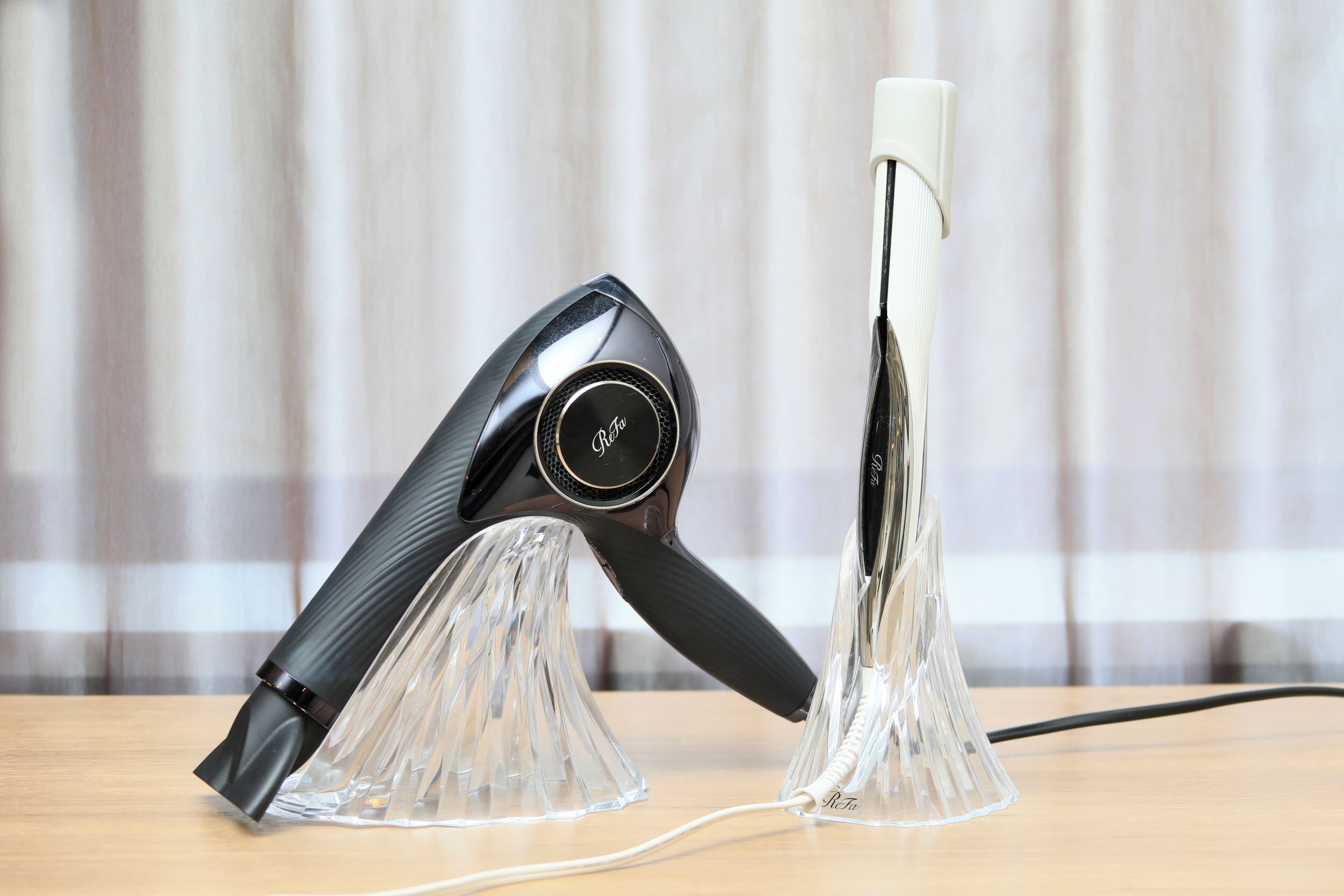 A hairdryer and a curling iron on a clear stand with a cord.