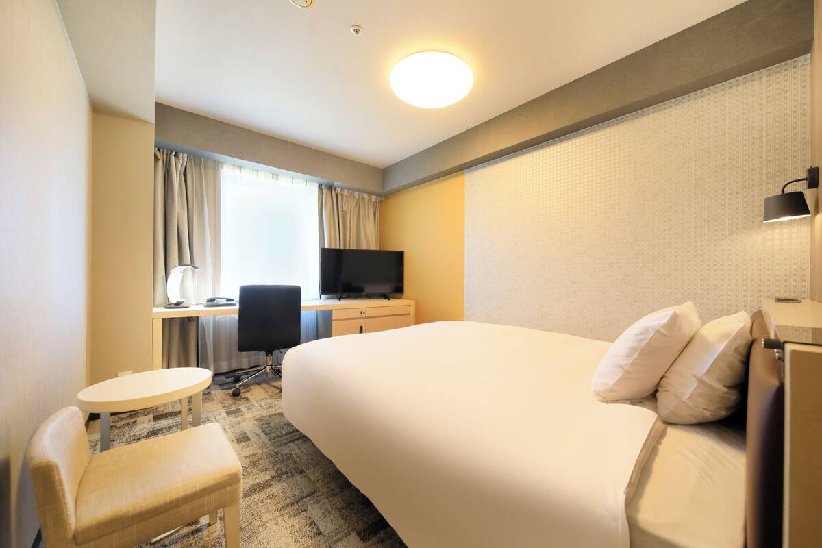 Une chambre d’hôtel avec un grand lit, un bureau avec un ordinateur, une chaise et un téléviseur.