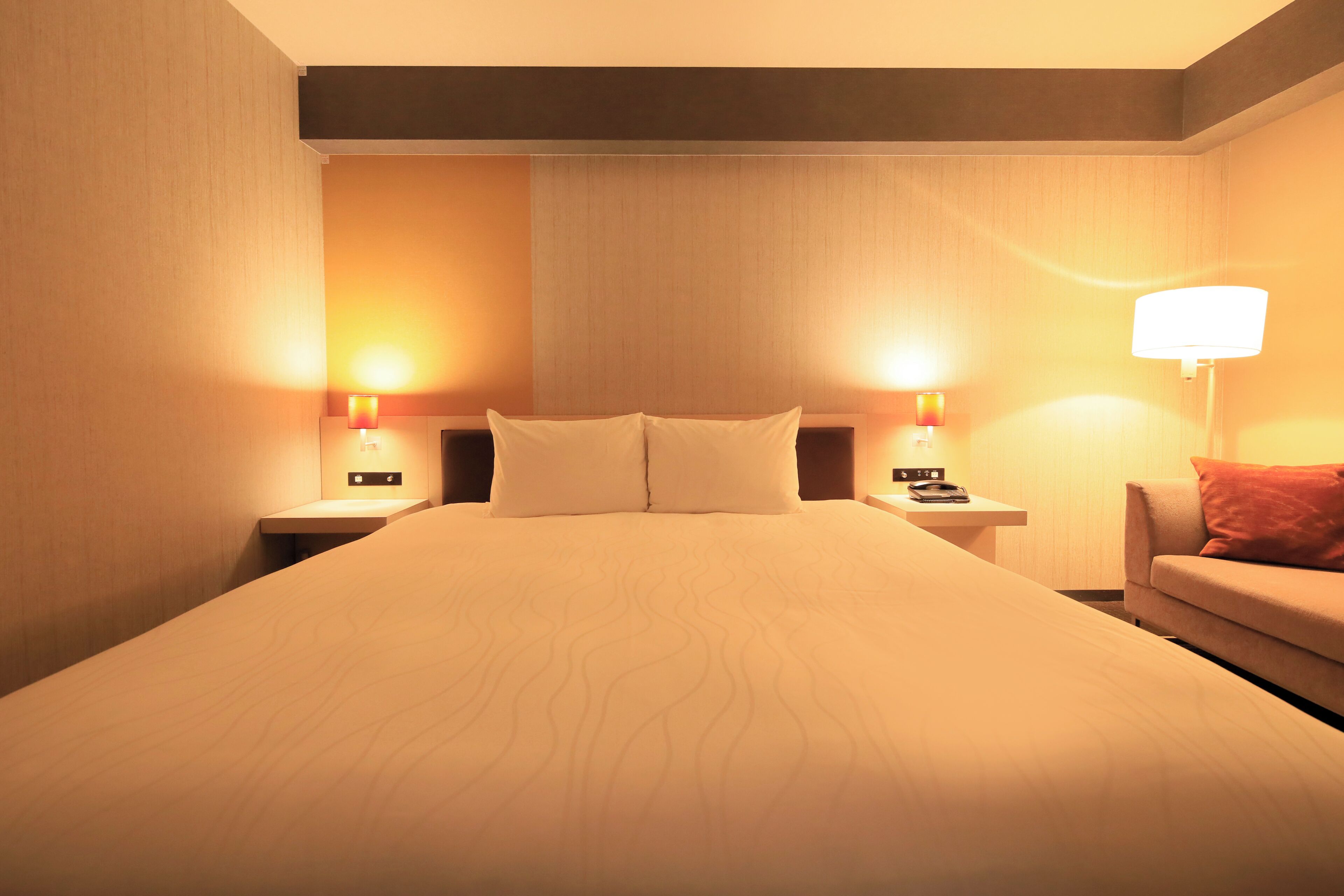 Een hotelkamer met een groot bed, twee nachtkastjes met lampen en een bank met een kussen.