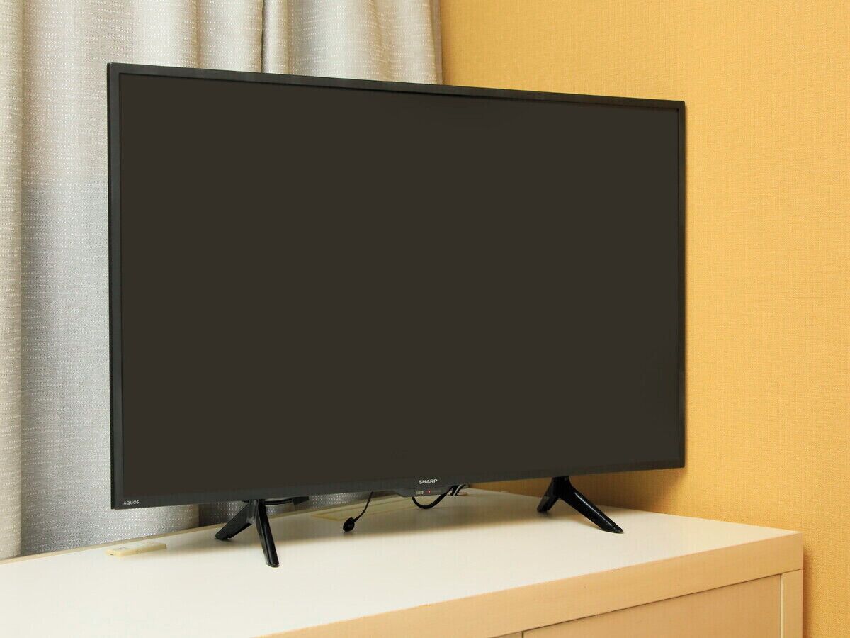 A flat-screen TV on a white stand against a yellow wall.