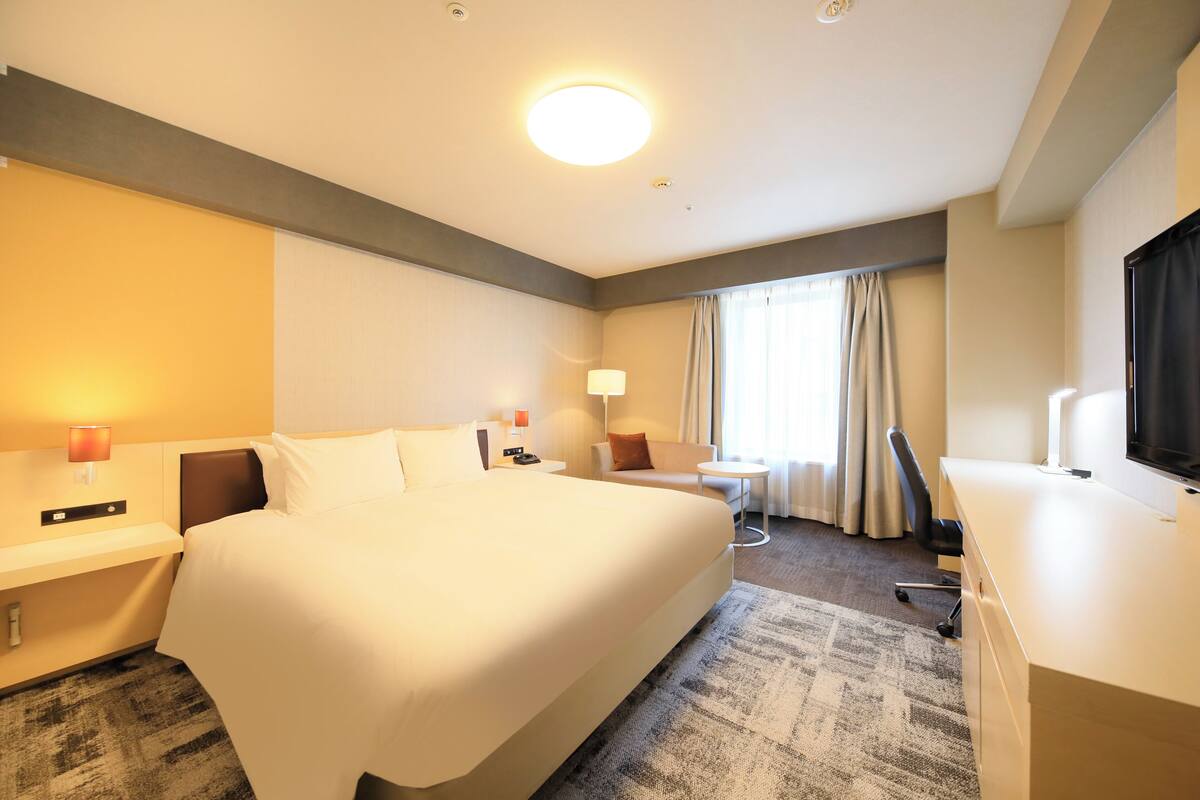 Une chambre d’hôtel avec un grand lit, un bureau, une chaise, une télévision et une petite table avec une lampe.