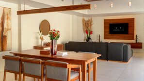 Un salon moderne avec une table à manger en bois, un canapé recouvert d’un tissu gris et un téléviseur à écran plat fixé au mur.