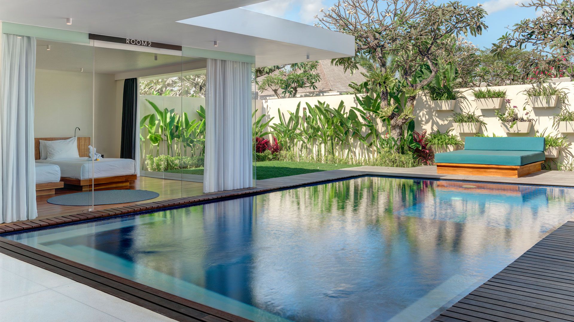 A modern hotel room with a glass wall, a pool, and a view of the garden.