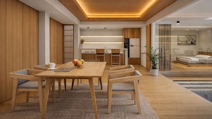 A modern interior with a wooden dining table, chairs, a fruit bowl, and a kitchen area.
