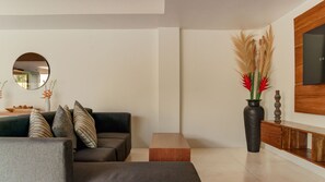 A modern living room with a sofa, a coffee table, a mirror, and a decorative vase with plants. - One Eleven Haven (Keroboken Kelod)