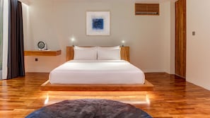 A bedroom with a wooden bed frame, white bedding, a small bedside table, a wall-mounted artwork, and a wooden floor. - One Eleven Haven (Keroboken Kelod)