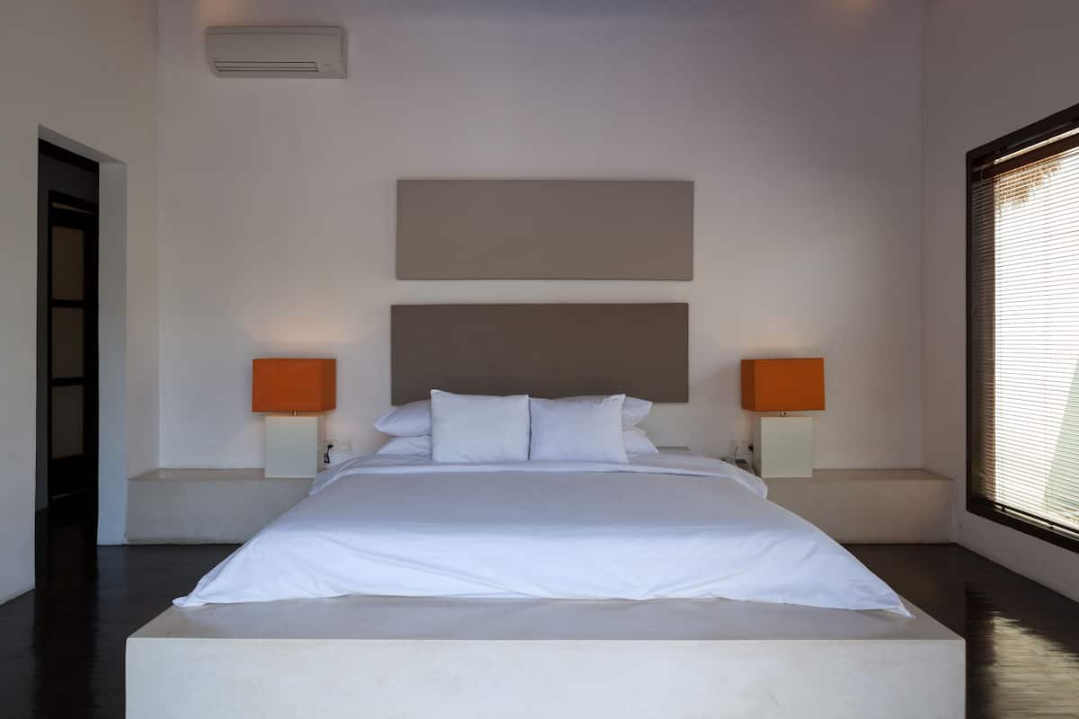 A modern bedroom with a large bed, two bedside lamps, and a window with blinds.