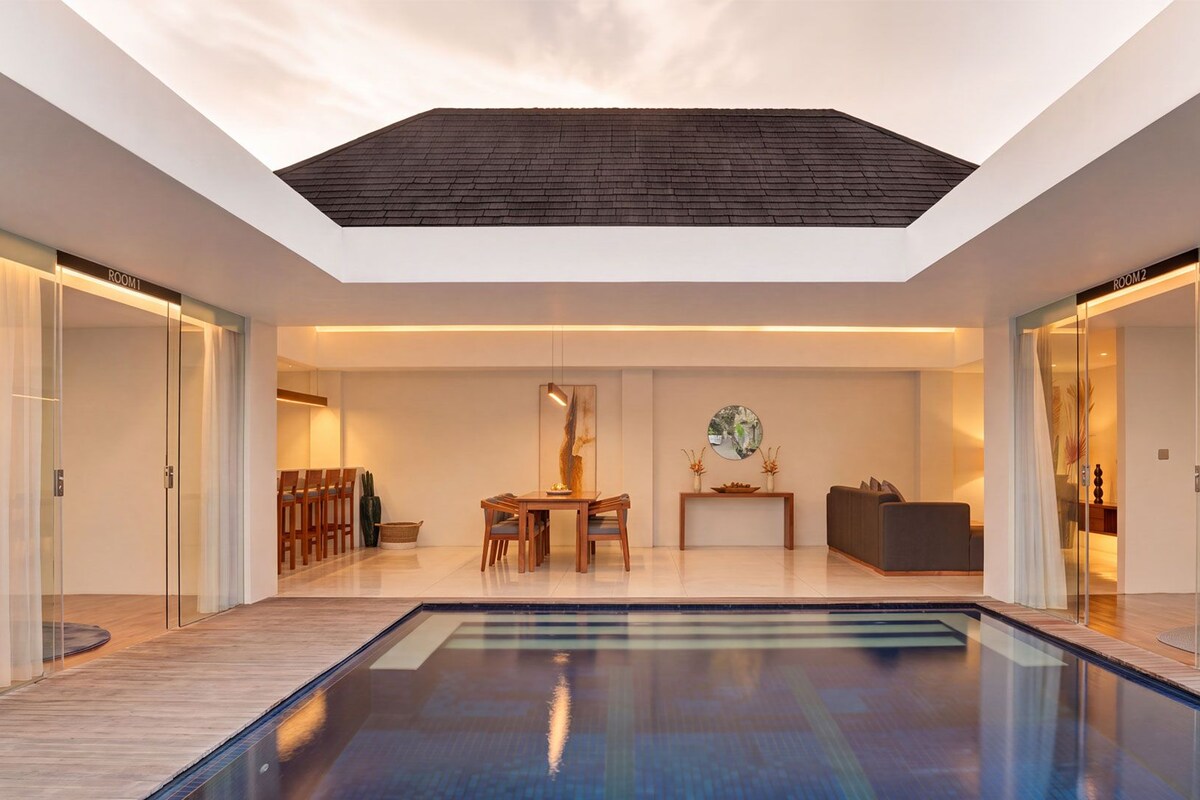 Un interior moderno con piscina central, comedor y sala de estar con vista al cielo a través de un tragaluz.