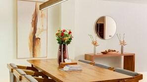 A dining area with a wooden table, cushioned chairs, a vase with flowers, a mirror, and a large abstract painting on the wall. - One Eleven Haven (Keroboken Kelod)