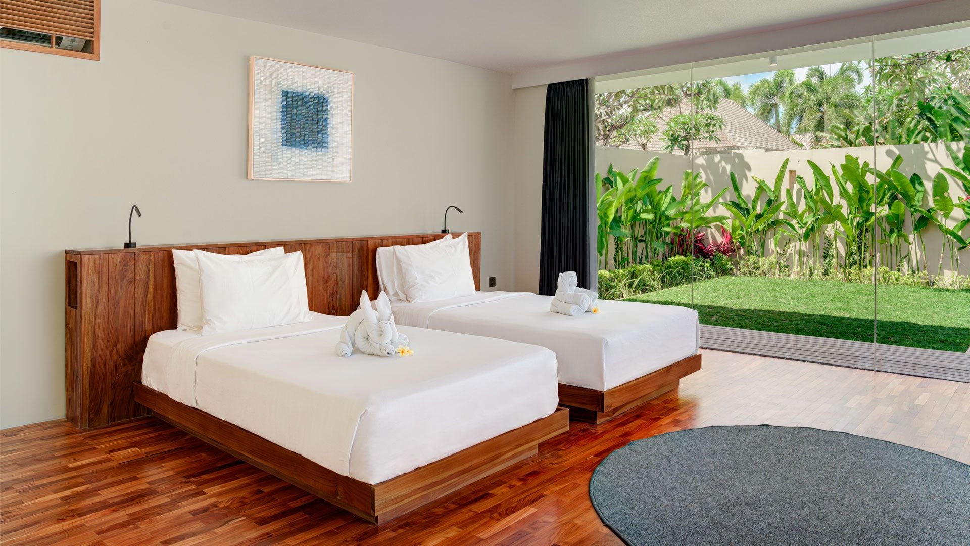 A hotel room with two beds, a wooden headboard, a framed picture, and a view of a garden.