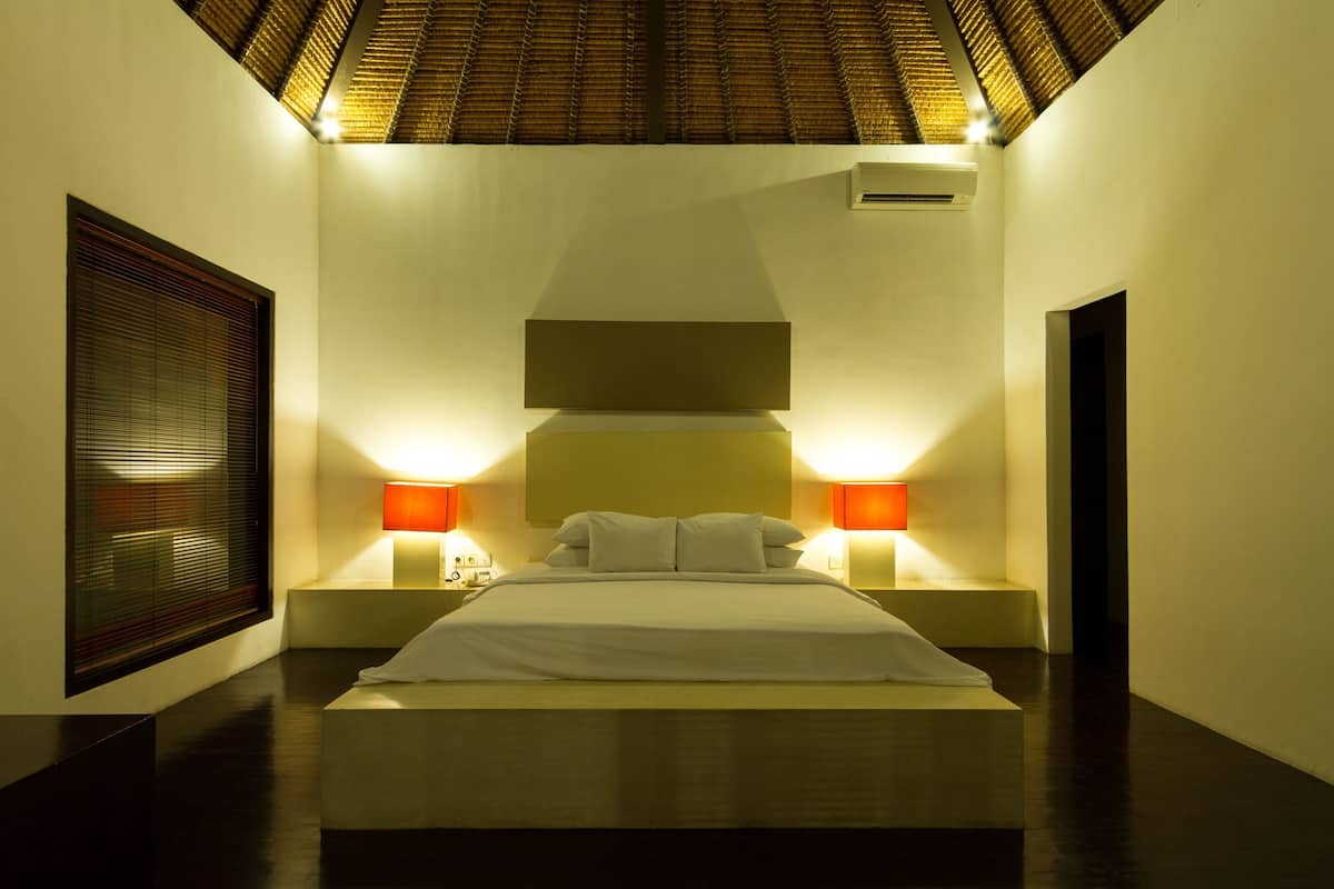 A bedroom with a bed, bedside lamps, a window with blinds, and a ceiling with a textured design.