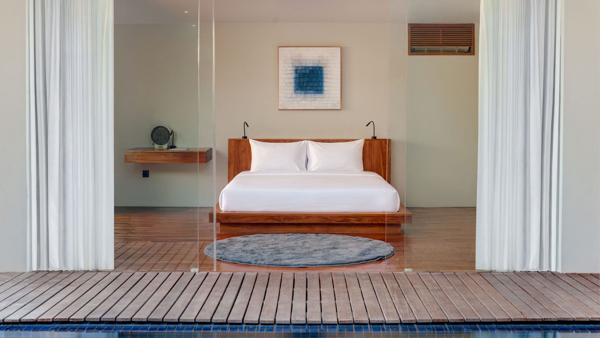 A bedroom with a wooden bed, white bedding, a round rug, a wall-mounted artwork, and a wooden floor.