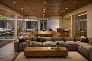 Uma sala de estar moderna com um amplo sofá seccional, uma mesa de centro de madeira e uma área de jantar com uma mesa comprida e cadeiras.