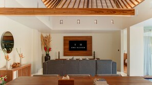 A modern living room with a wooden ceiling, a grey sofa, a wooden coffee table, and a wall-mounted TV displaying 'ONE ELEVEN'. - One Eleven Haven (Keroboken Kelod)