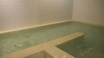 A small, rectangular hot tub with a wooden edge, surrounded by white tiled walls.