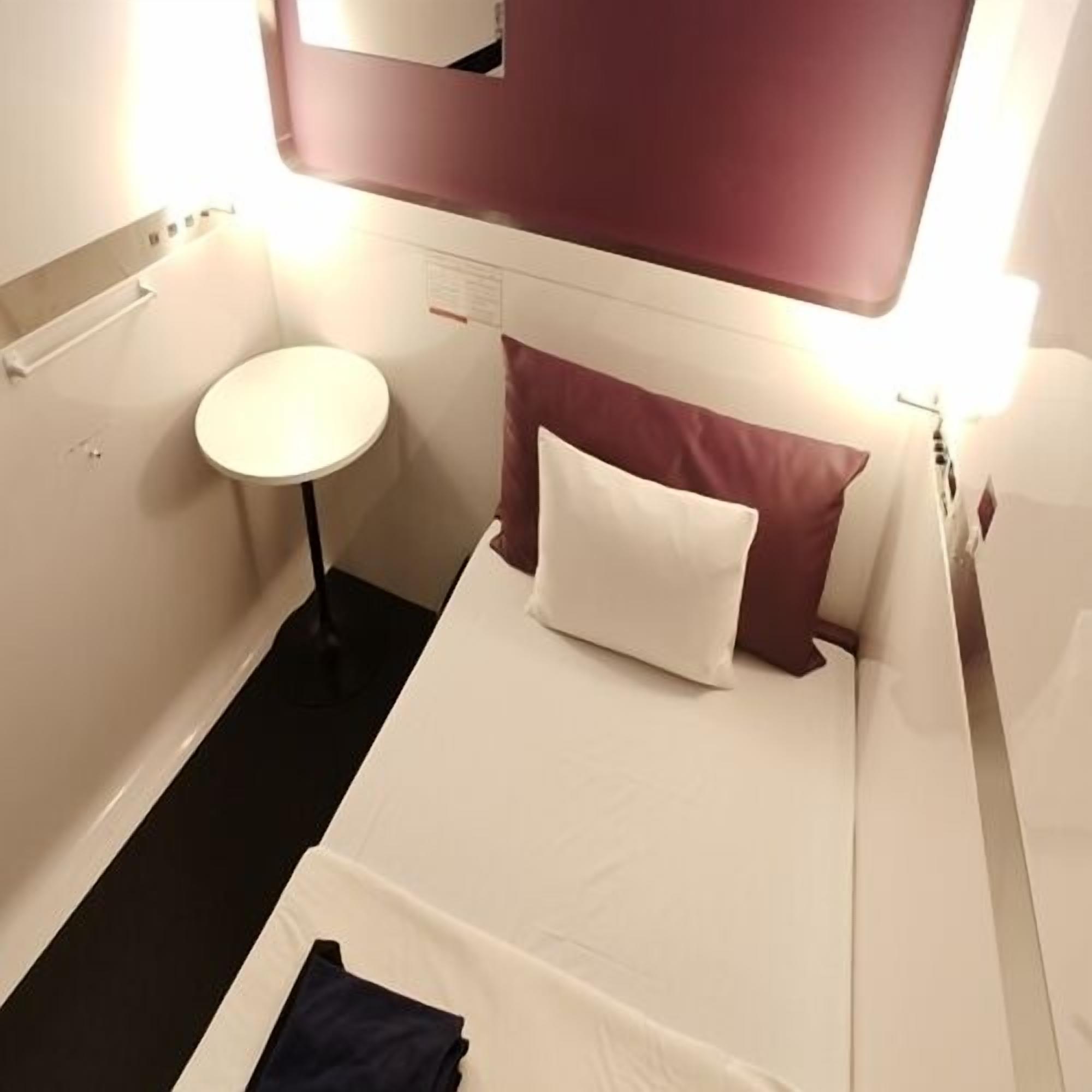 Une petite chambre avec un lit simple, une table ronde, un miroir et un mur d’accent de couleur rouge.