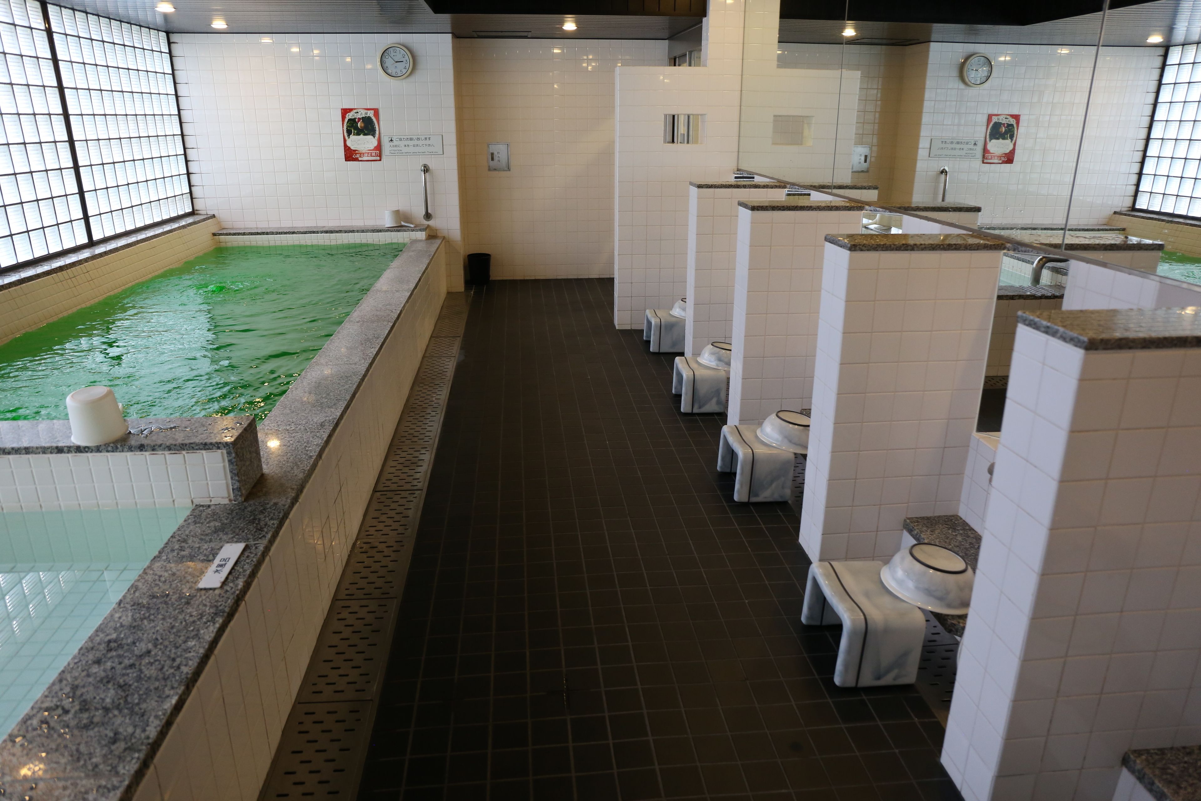Een openbaar badgedeelte met een groot binnenzwembad, meerdere toiletten en een betegelde vloer.