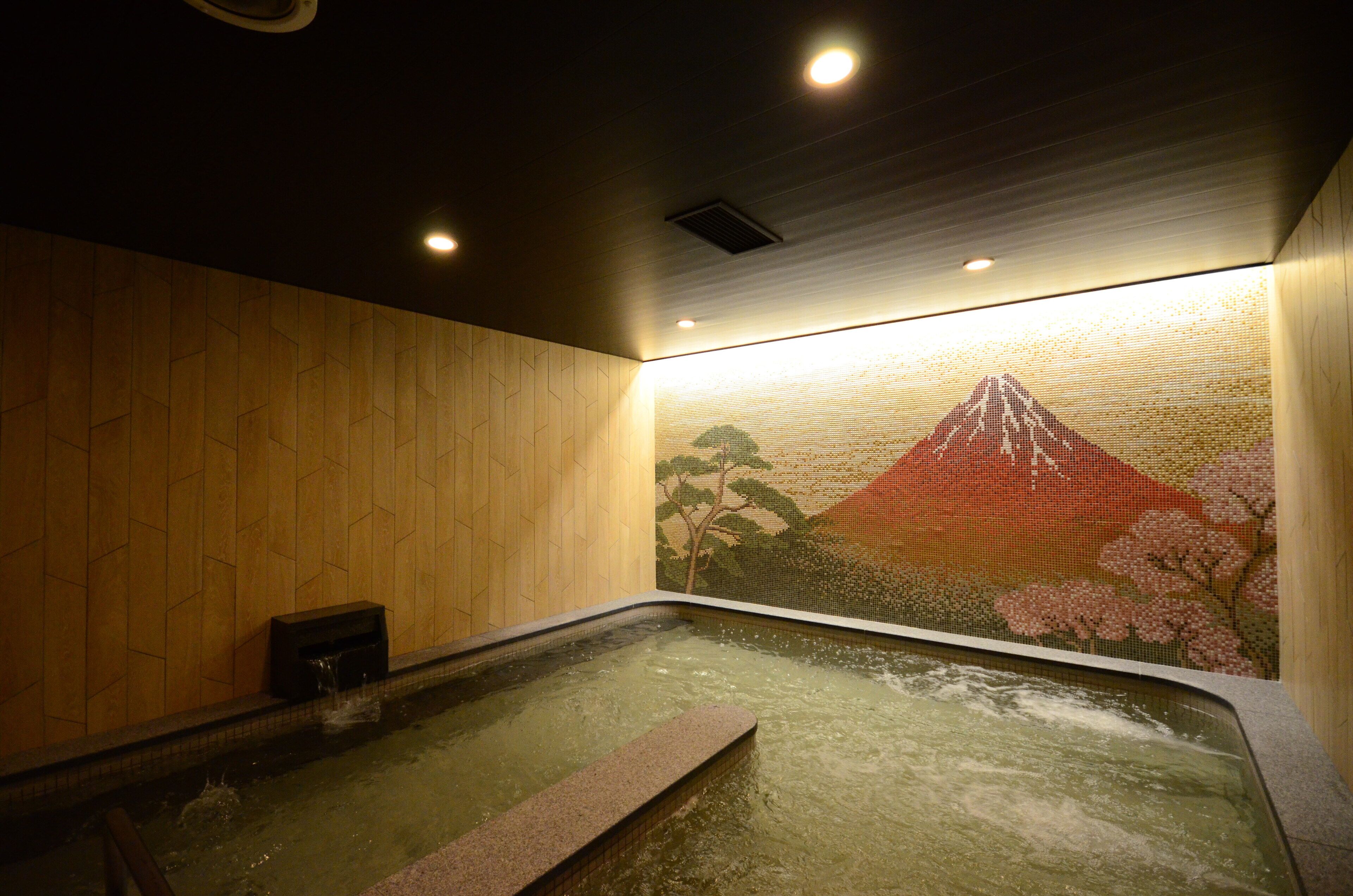 A hot spring bath with a wooden wall and a mural of a mountain and cherry blossoms.