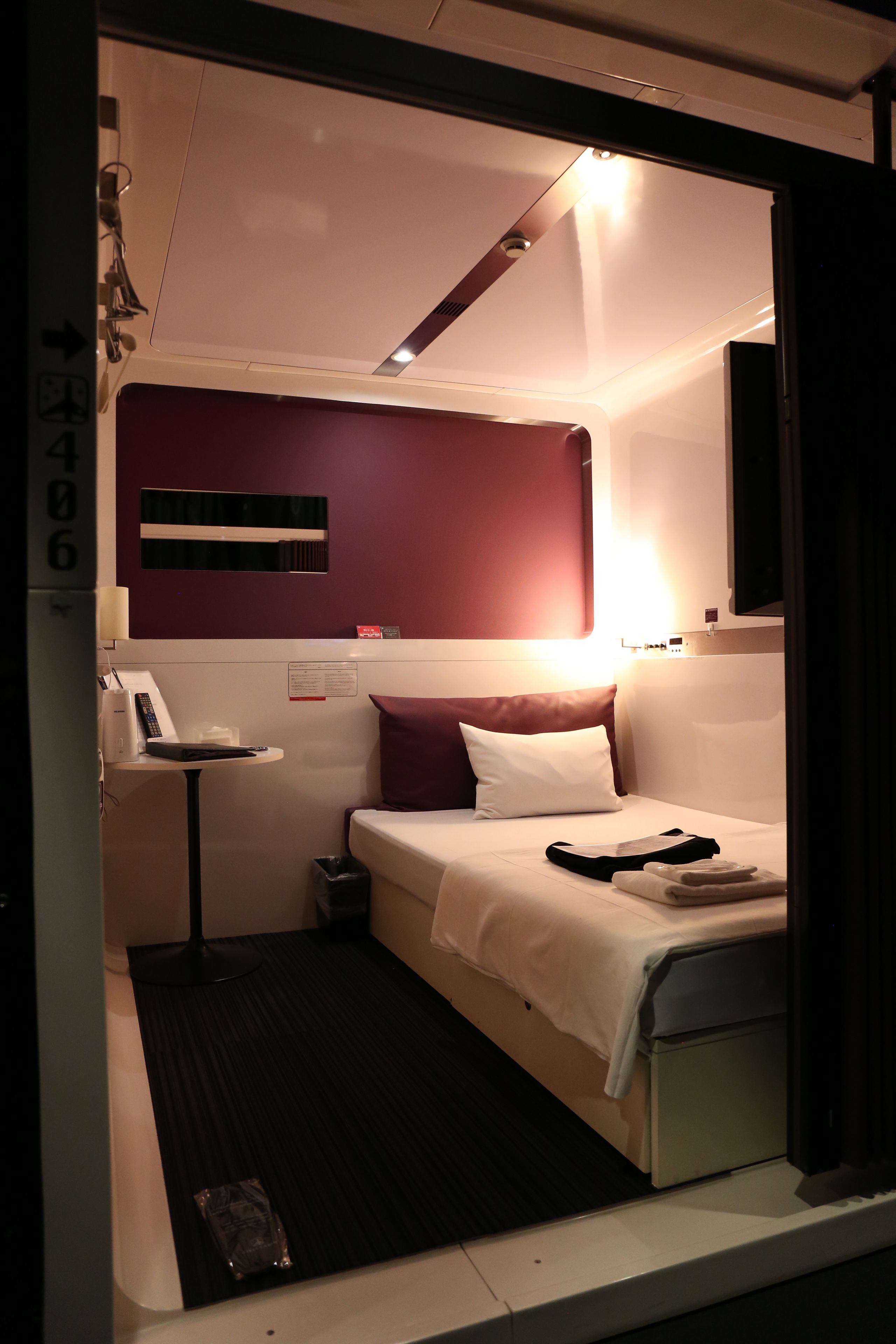 Una habitación de hotel pequeña con cama, mesita de noche y un escritorio con lámpara.