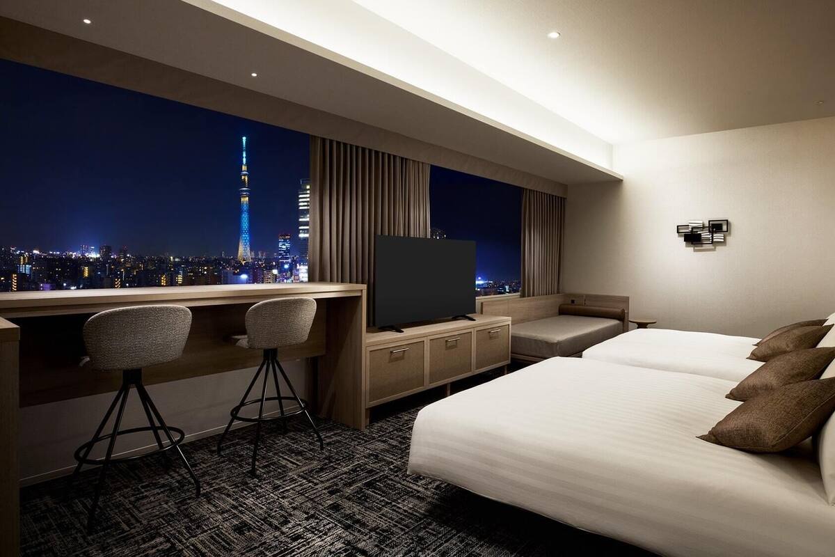 A hotel room with a large bed, a desk with a chair, a TV, and a city view.